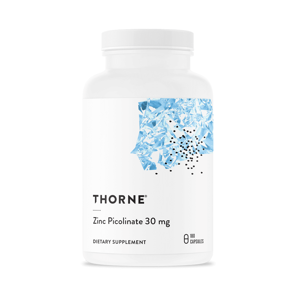 Thorne Zinc Picolinate bottle next to a weekly pill organizer and glass of water on a kitchen table