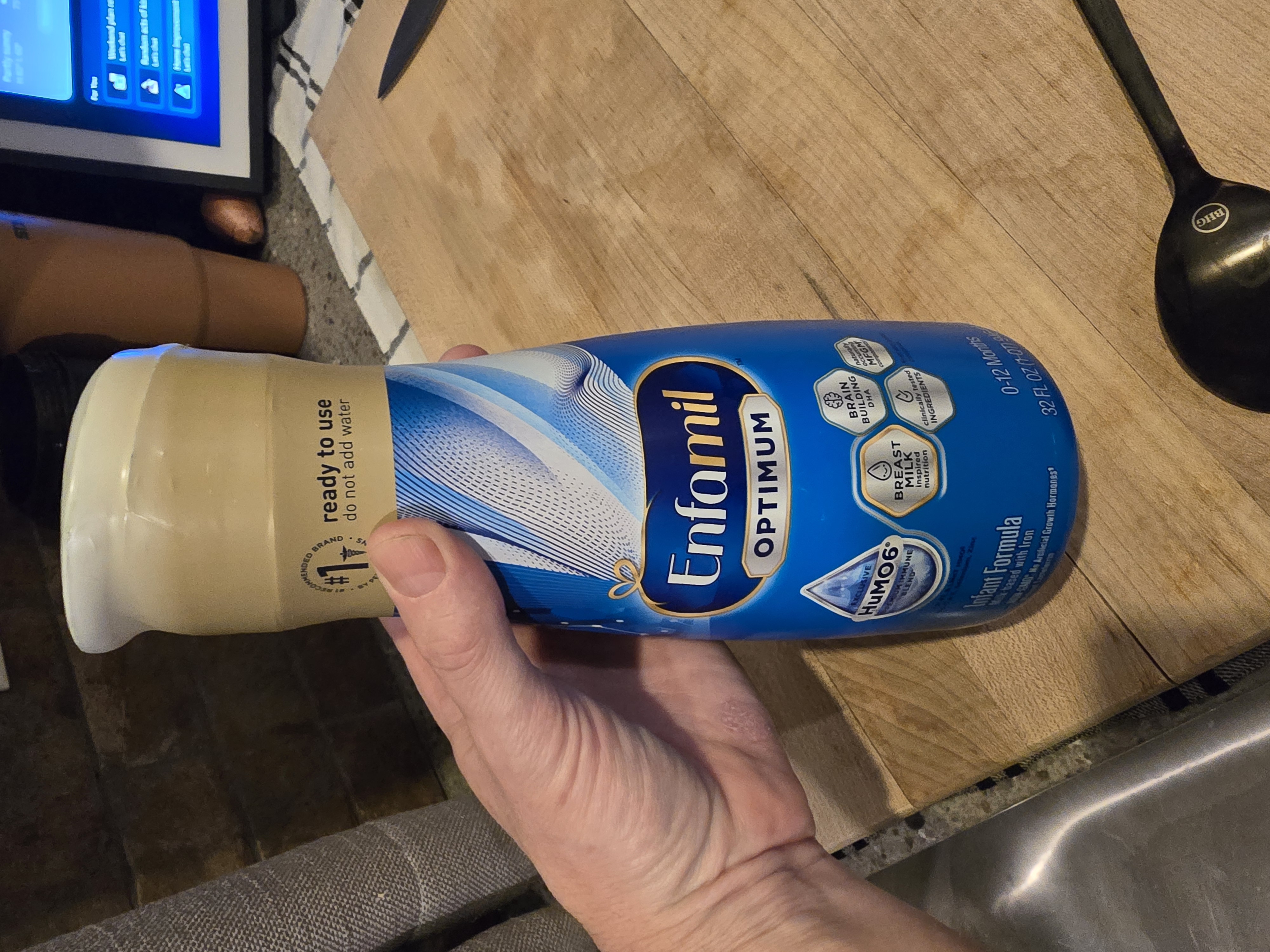 Three Enfamil Optimum single-serve bottles on a wooden nightstand with warm lamp lighting