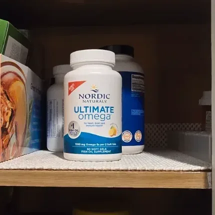 Two golden fish oil soft gel capsules next to a glass of water on a sunlit kitchen counter