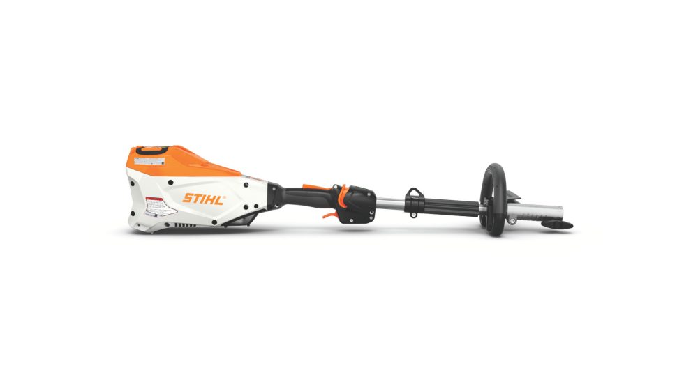 STIHL KMA 135 R trimmer attachment cutting through tall grass along a wooden fence line in afternoon light
