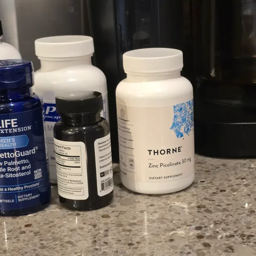 Multiple supplement bottles including Thorne Zinc Picolinate arranged on a wooden desk in warm light.