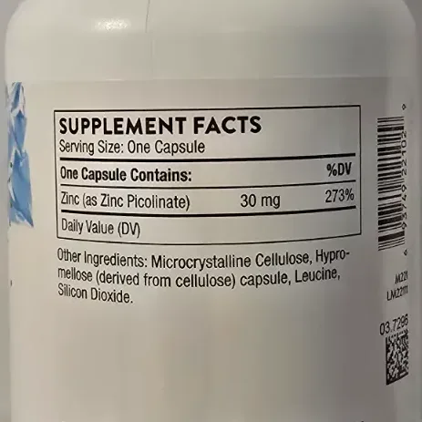 Thorne Zinc Picolinate capsules spilling from a white supplement bottle onto a warm wooden surface.