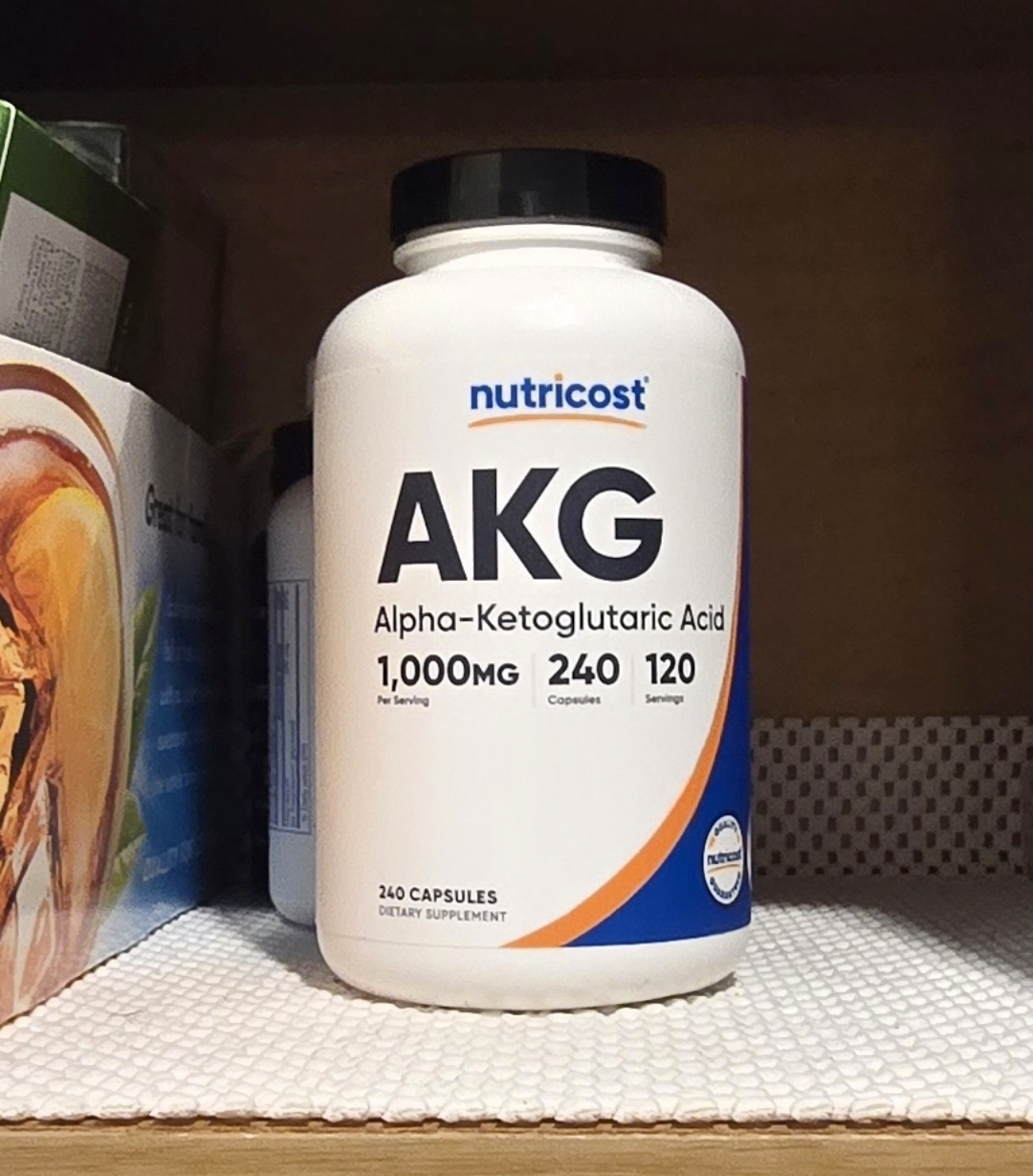 Two white AKG capsules next to a Nutricost supplement bottle on a wooden surface with natural side lighting