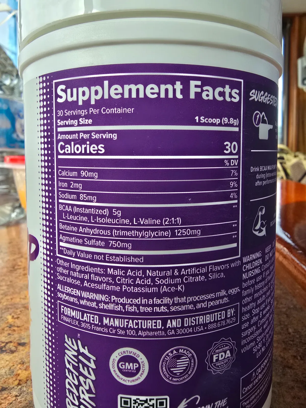BCAA supplement tub and scoop next to a small stack of cash on a wood surface
