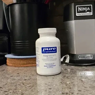 Pure Encapsulations supplement bottle next to a daily supplement organizer tray on a warm wood countertop