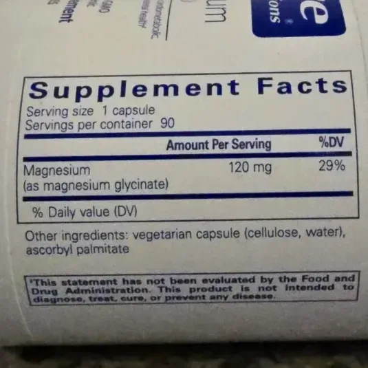 Open vegetarian supplement capsules showing white magnesium glycinate powder on a natural wood surface