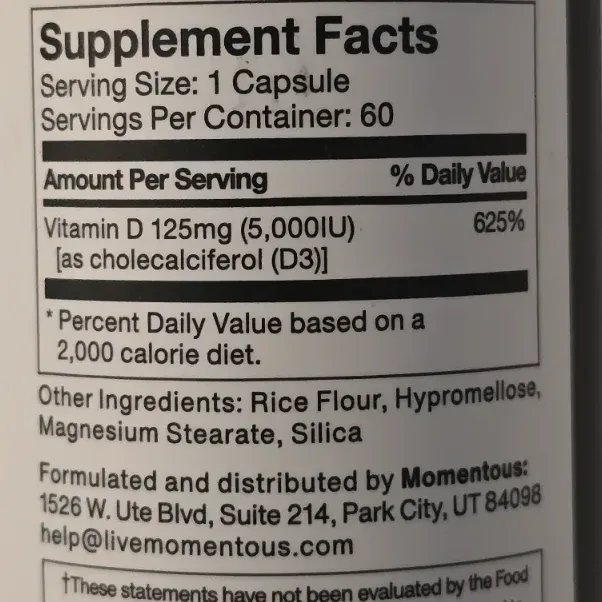 Small Momentous Vitamin D3 vegetable capsules next to the supplement bottle on a white surface.