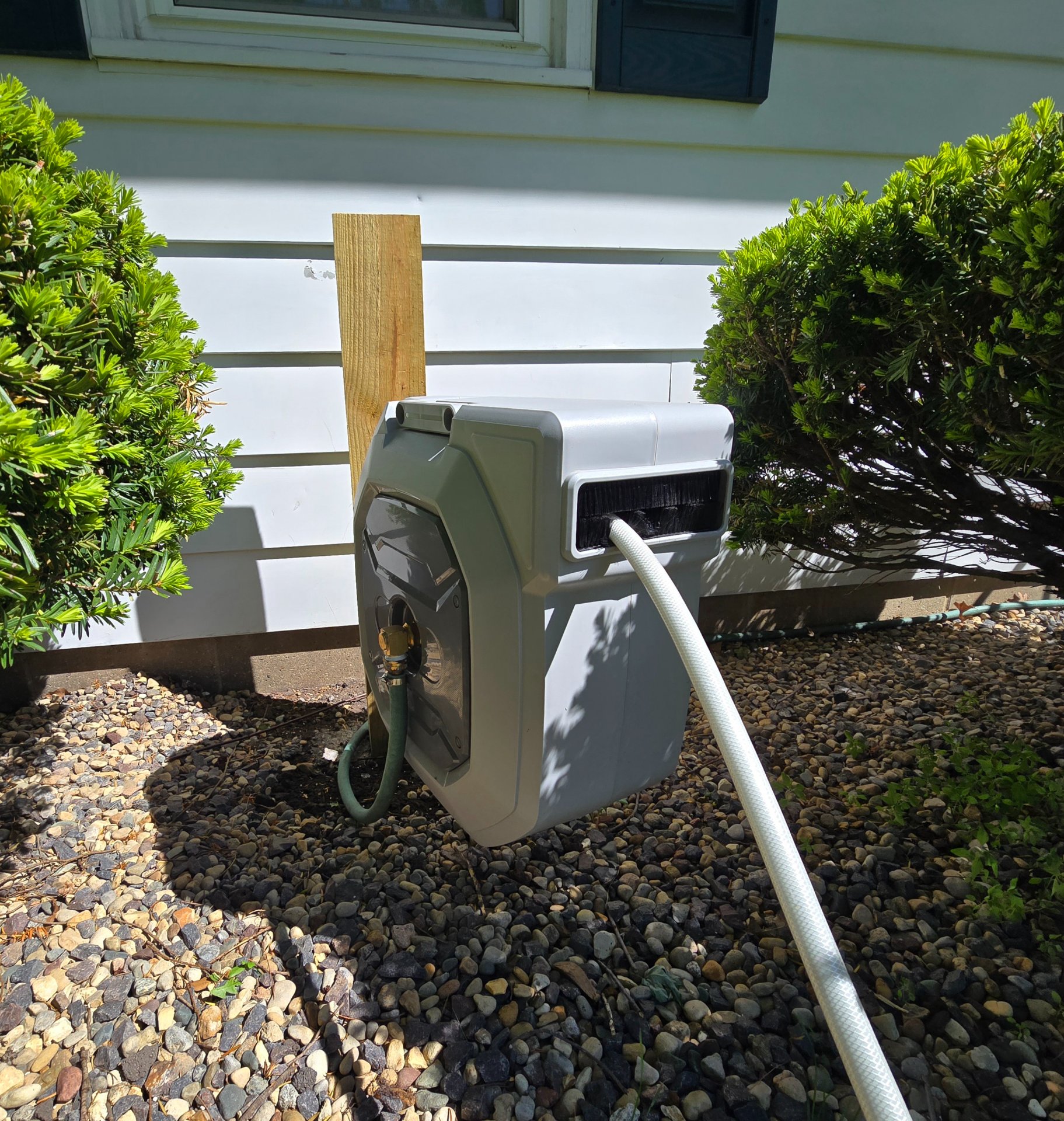 Hozereel hose reel mounted on front yard house exterior with garden beds visible in background