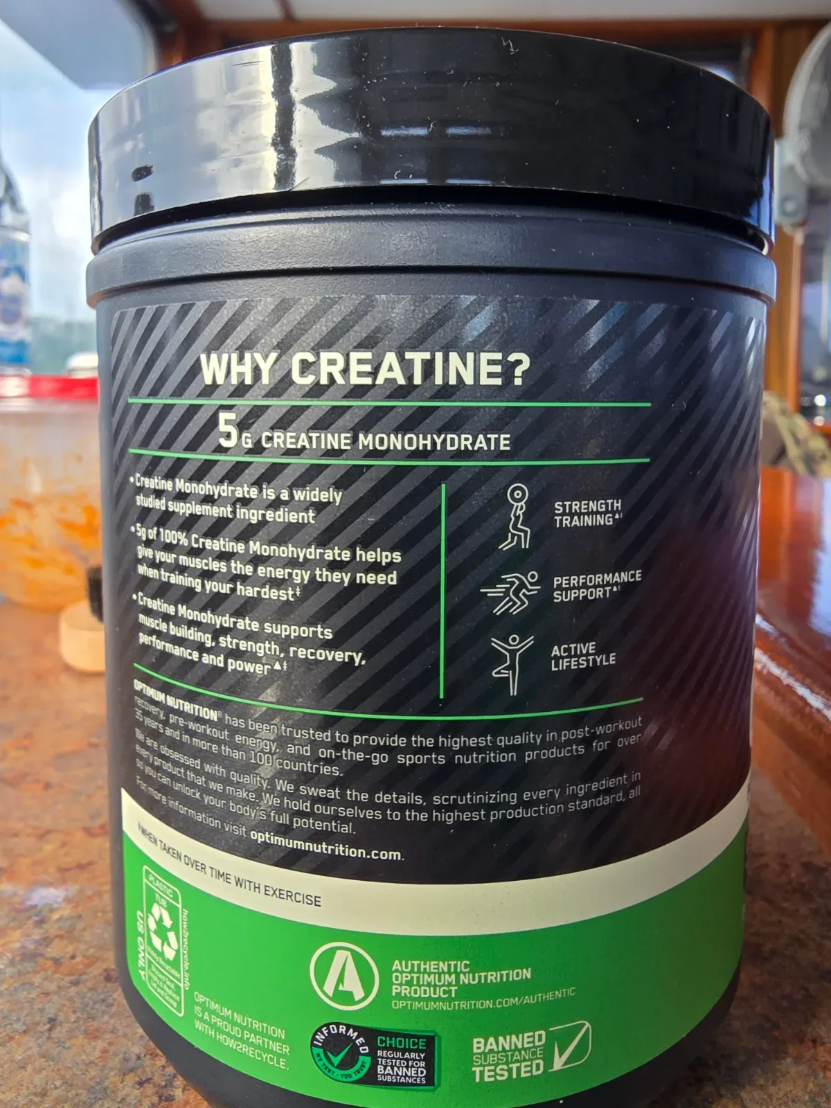Overhead view of a creatine powder tub beside cash and a receipt on a wood surface