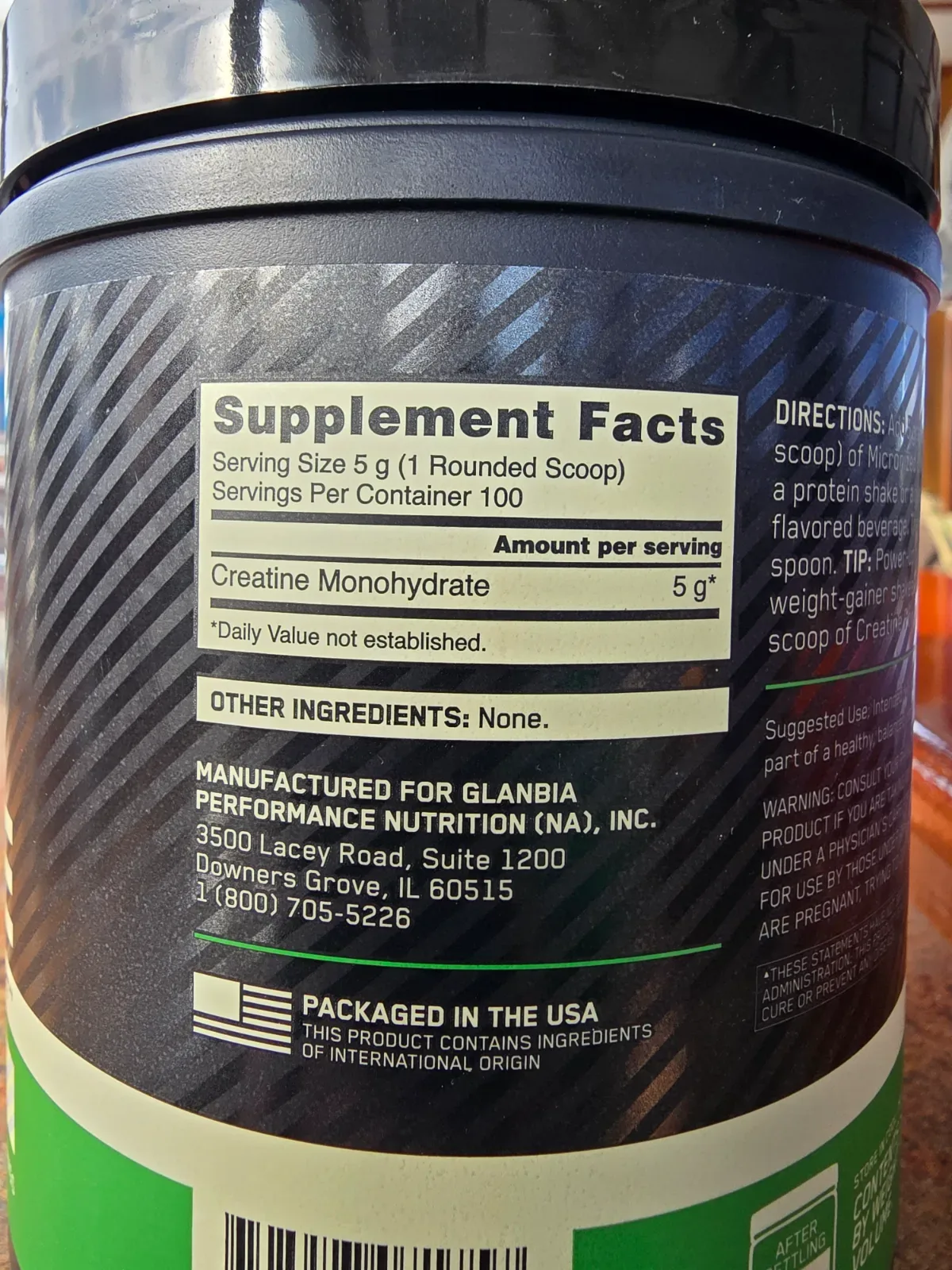 White supplement tub of creatine monohydrate powder with a scoop resting on the open lid